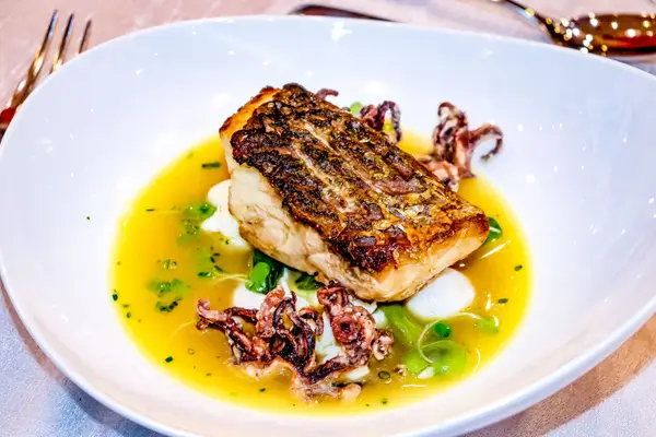 Un filet de poisson grillé dans un bouillon safrané, vu de dessus.