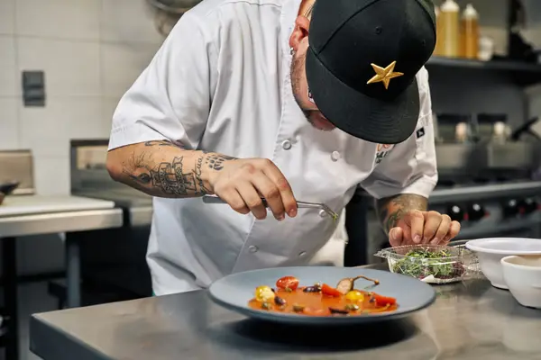 Un cuisinier qui dresse une assiette à la pince, en cuisine.